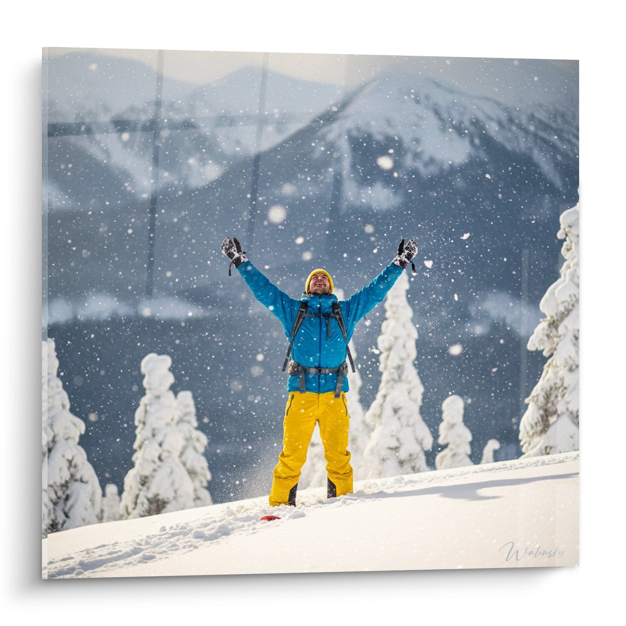 Skifahrer in blauer Jacke und gelber Hose jubelt mit erhobenen Armen im Schneesturm vor Bergkulisse