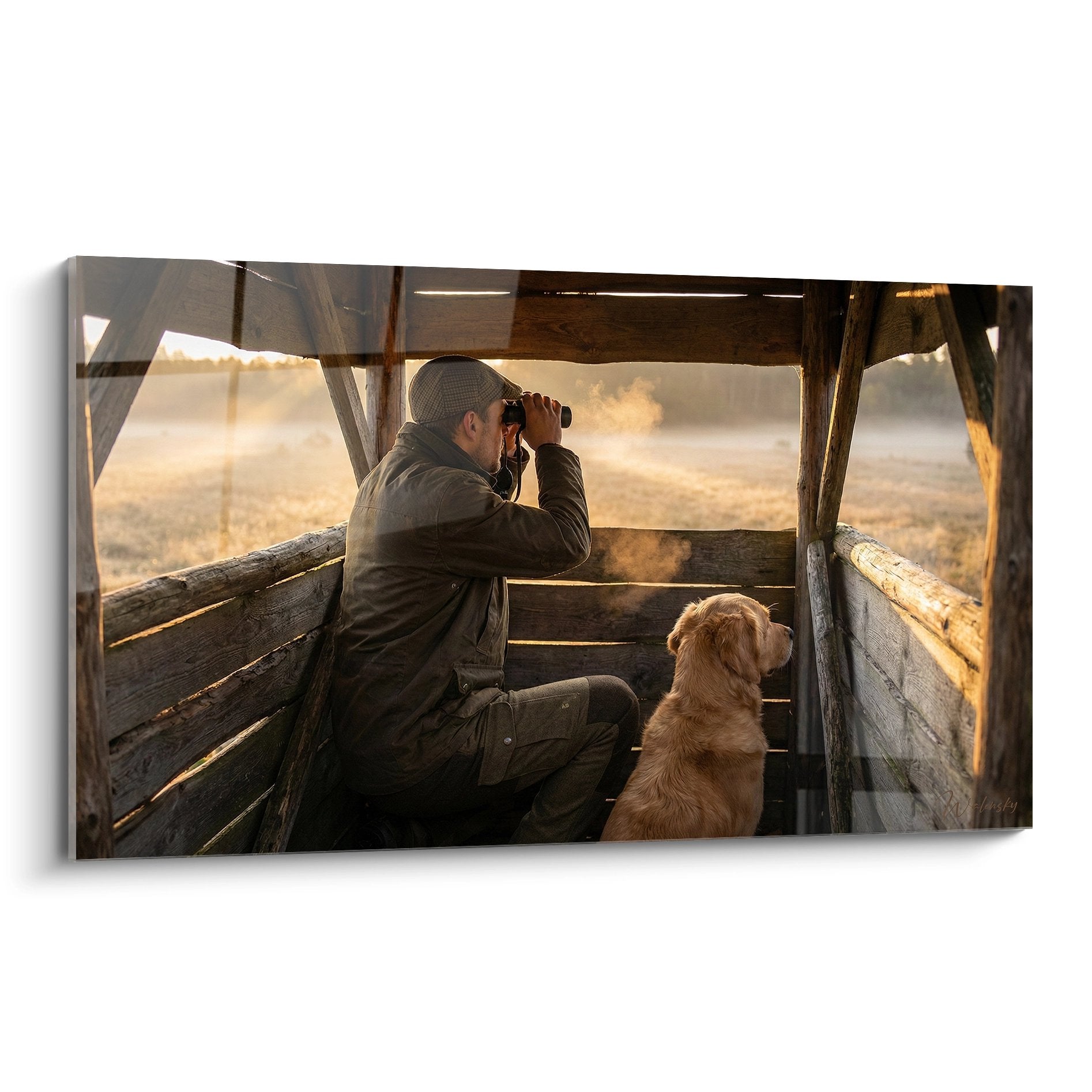 Jäger mit Fernglas und Jagdhund im Holz-Hochsitz bei goldenem Morgenlicht mit nebligem Hintergrund